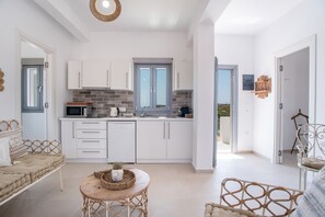A modern kitchen with white cabinets, a microwave, and a sink. There is a dining area with a wicker table and chairs.