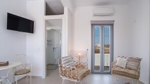 Une pièce avec un téléviseur, deux fauteuils en osier, une table, une lampe et une porte-fenêtre donnant sur un balcon.