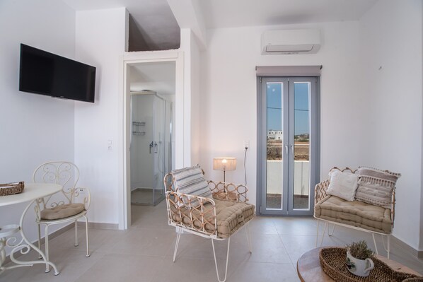 A room with a TV, two wicker chairs, a table, a lamp, and a balcony door.
