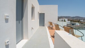 Un balcon moderne offrant une vue sur des collines lointaines, avec une porte et deux chaises.