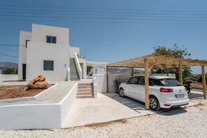 Ein modernes, weißes Gebäude mit einem Auto, das unter einer Holzpergola abgestellt ist.