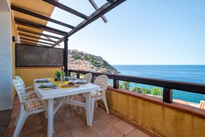 A balcony with a table and chairs, overlooking a coastal town and the sea. - Holiday Home 'The Terrace Above The Sea' with Sea View, Private Terrace & Air Conditioning (Castelsardo)