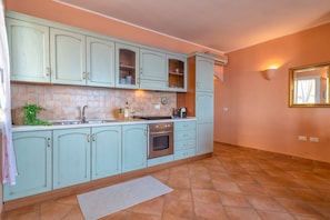 Eine Küche mit hellblauen Schränken, einer gefliesten Spritzschutzwand, einem Edelstahlbackofen und einem kleinen Teppich auf dem Boden.