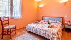 Een slaapkamer met een bed, een stoel, een nachtkastje en een raam met gordijnen.