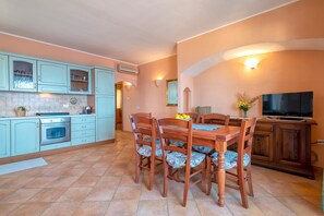Une cuisine avec des armoires de couleur turquoise, une table à manger avec des chaises à motifs floraux et un téléviseur sur le côté droit.