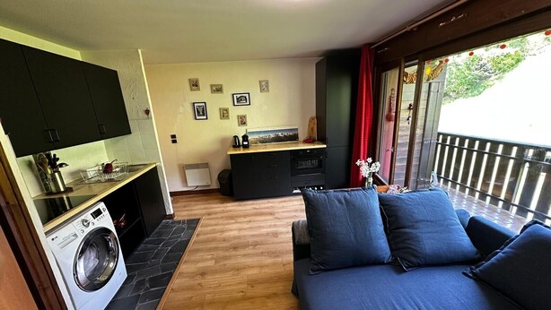 Un espace de vie compact comprenant une kitchenette, un lave-linge, un canapé et un balcon avec vue.