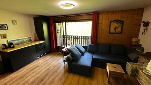 Un salon avec un plancher en bois, un canapé, une petite table et un coin cuisine comprenant un comptoir et des placards.