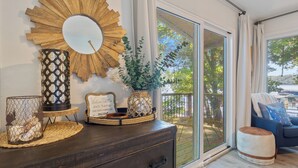 Een moderne woonkamer met een donkere houten dressoir, decoratieve spiegels en uitzicht op een balkon met buitenmeubilair.