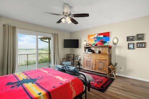 A bedroom with a bed, a ceiling fan, a TV, a wooden cabinet, and a balcony with curtains. - Luxury Lake Life - Boat Dock, Outdoor Kitchen, Basketball Court, Game Room & Bar (Lago Vista)