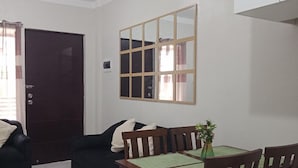 A living room with a dark-colored sofa, a dining table with four chairs, and a large mirror on the wall. - Antonioville Subdivision (Mandaue)
