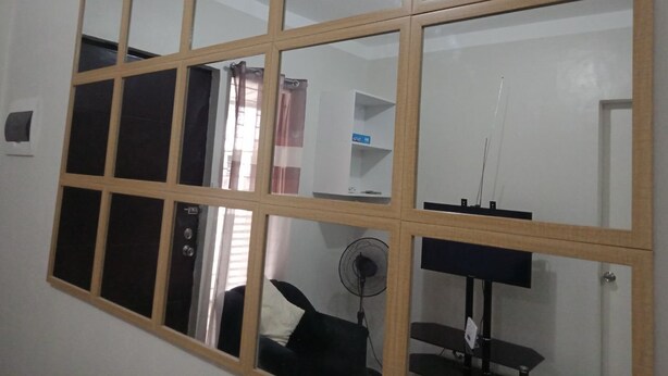 A room with a large window divided into nine panes, a black desk, a chair, a standing fan, and a white wall with a door. - Antonioville Subdivision (Mandaue)