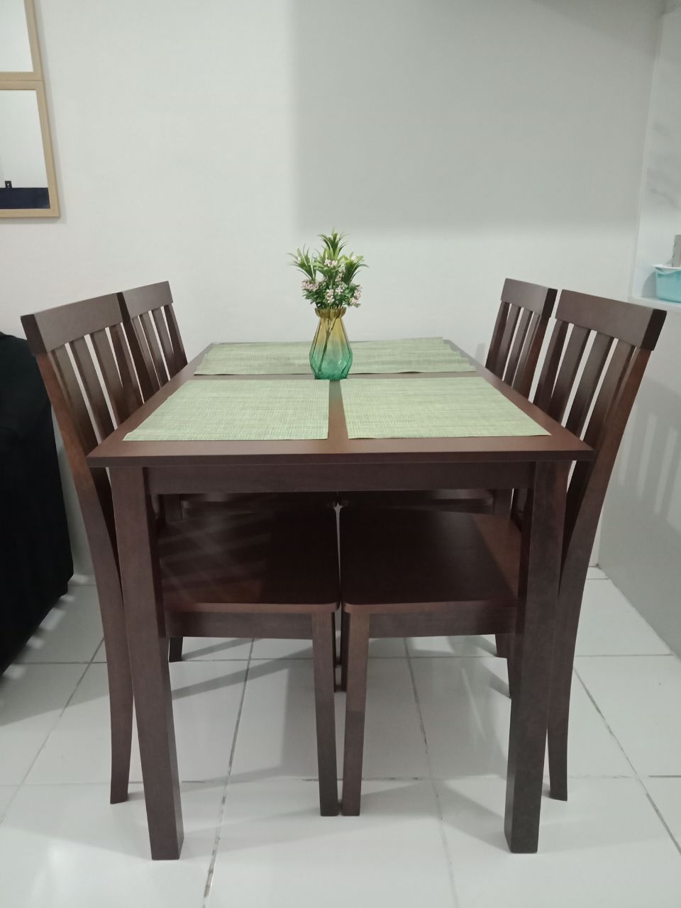 A dining table with four chairs, a vase with flowers, and a green placemat.