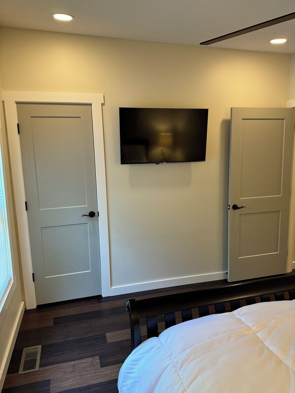 Un dormitorio con una cama, un televisor de pantalla plana en la pared y dos puertas.