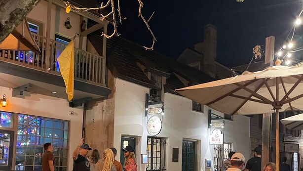 Un espacio al aire libre para comer con mesas y sillas de madera, un letrero que indica un restaurante jardín y un edificio con balcón.
