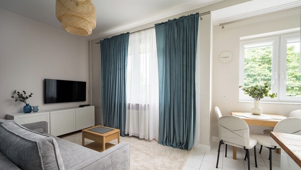 A modern living room with a grey sofa, a wooden coffee table, a flat-screen TV on a white cabinet, and a dining area with a wooden table and chairs. - Wola Ratusz Homely Apartment (Warszawa)