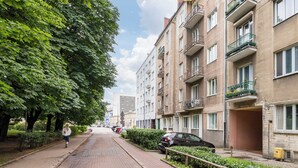A residential street with apartment buildings, parked cars, and a pedestrian walking on the sidewalk. - Wola Ratusz Homely Apartment (Warszawa)