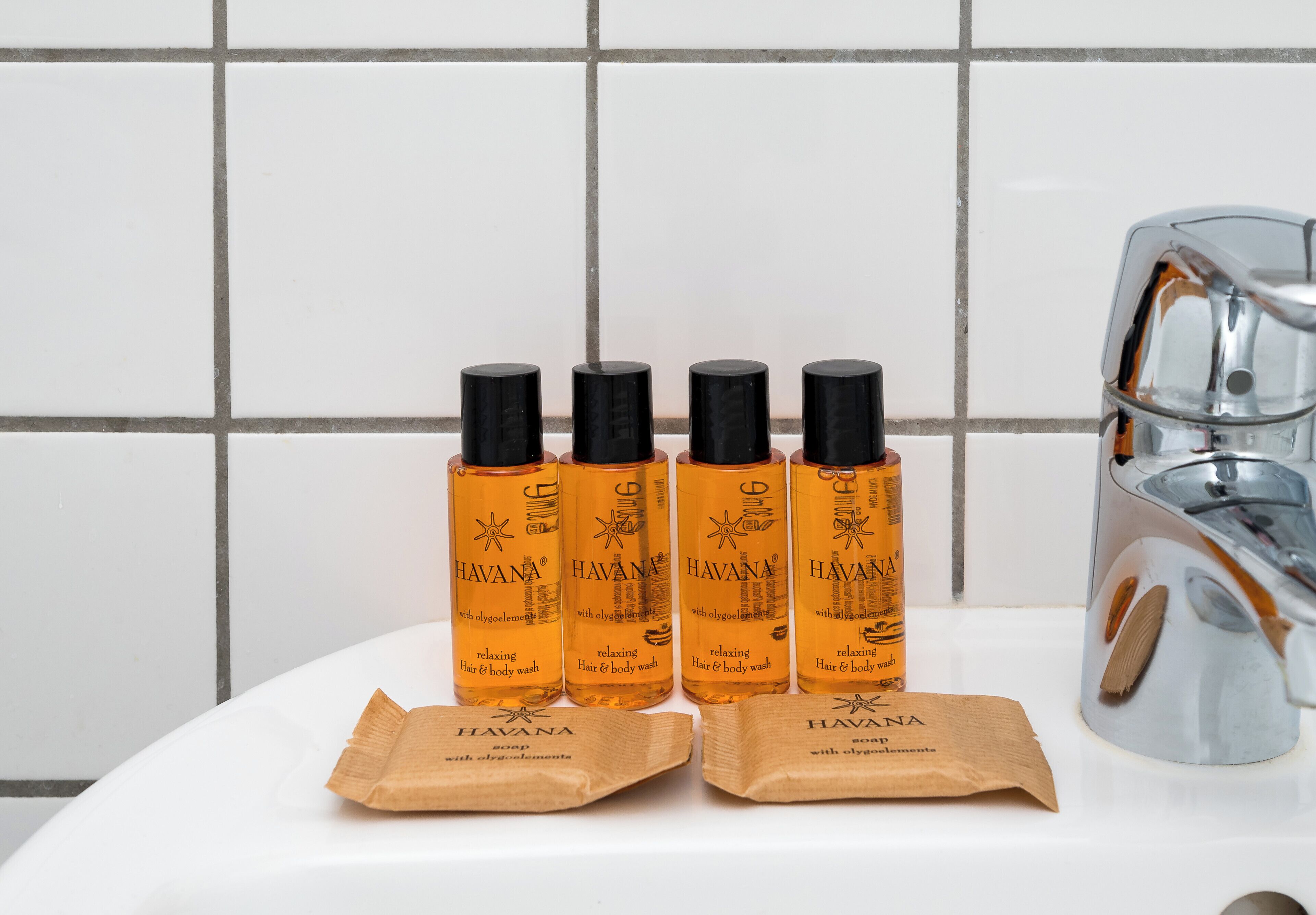 Quatre bouteilles de gel douche Havana et deux sacs en papier brun sur une surface blanche.