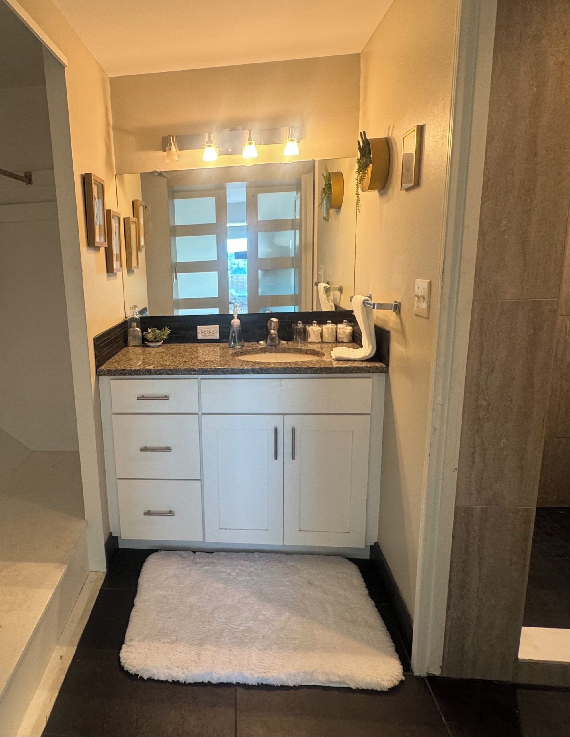 Une salle de bain avec un meuble-lavabo blanc, un grand miroir et une serviette blanche sur le sol.
