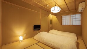 A traditional Japanese room with tatami flooring, a bed with white bedding, a mounted television, and a sliding shoji screen. - Saju Kyoto (Kyoto)