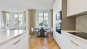 A modern kitchen with white cabinetry, a dining table with chairs, and a view of palm trees through large windows.