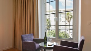 A room with a large window, two chairs, a small table, a bottle, and two wine glasses.
