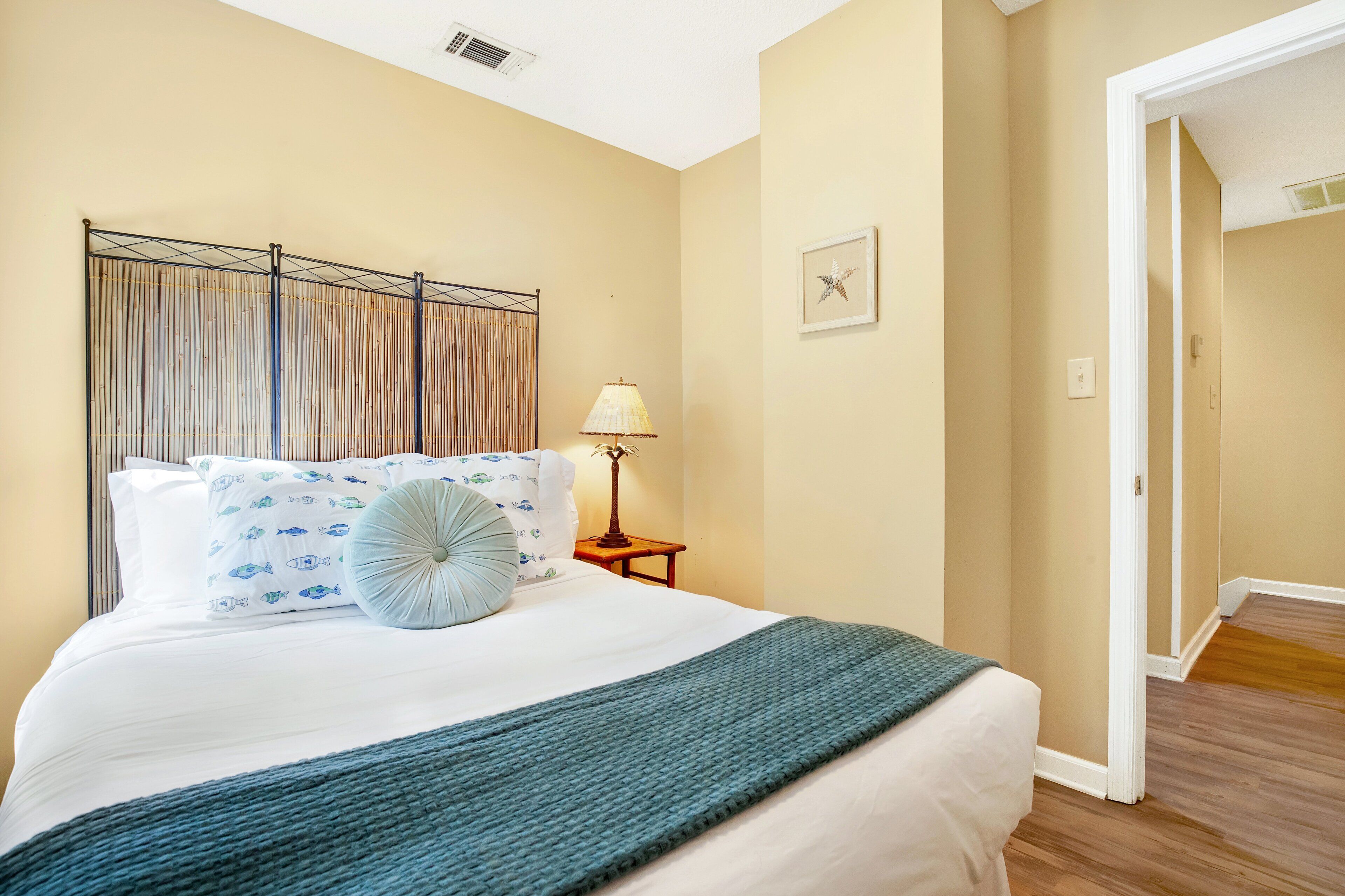A neatly made bed with a blue throw blanket, a decorative pillow, and a wall-mounted light fixture.
