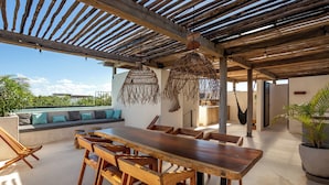 An outdoor dining area with a long wooden table and chairs, a thatched ceiling, and a view of the surrounding landscape. - Tuané Tulum (Tulum)