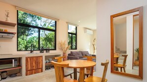 A modern kitchen with wooden cabinets, a dining table, and chairs. There is a large window with a view of trees. - Tuané Tulum (Tulum)