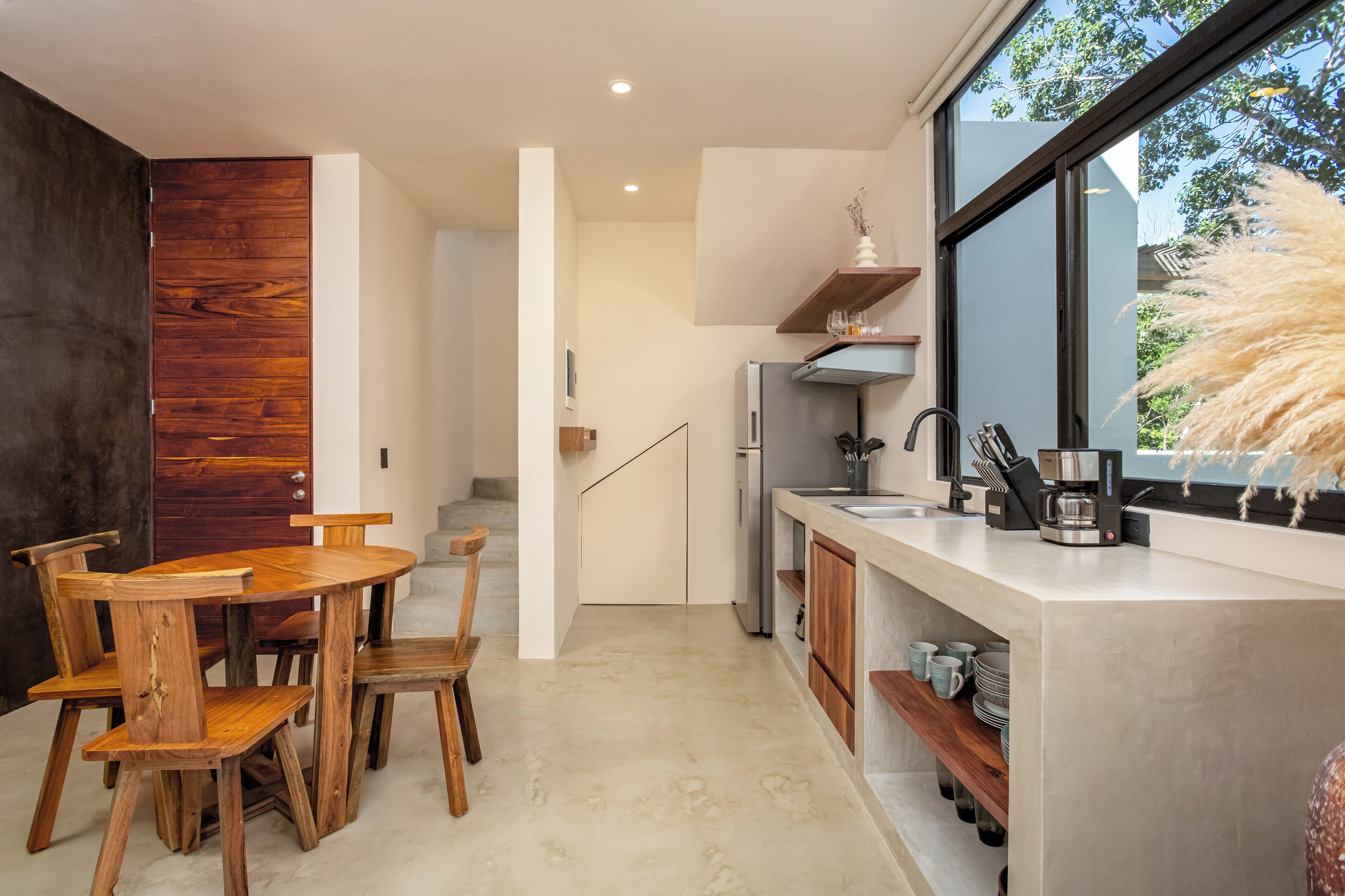 Una cocina moderna con una mesa y sillas de madera, horno empotrado y un ventanal con vistas a árboles.
