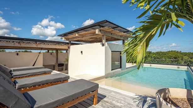 A modern outdoor pool area with lounge chairs, a pergola, and a view of the surrounding landscape. - Tuané Tulum (Tulum)