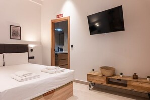 Habitación de hotel con cama, televisor montado en la pared, armario de madera y señalización de salida.