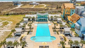 An aerial view of a resort with a central swimming pool, multiple lounge areas, and beachfront properties.