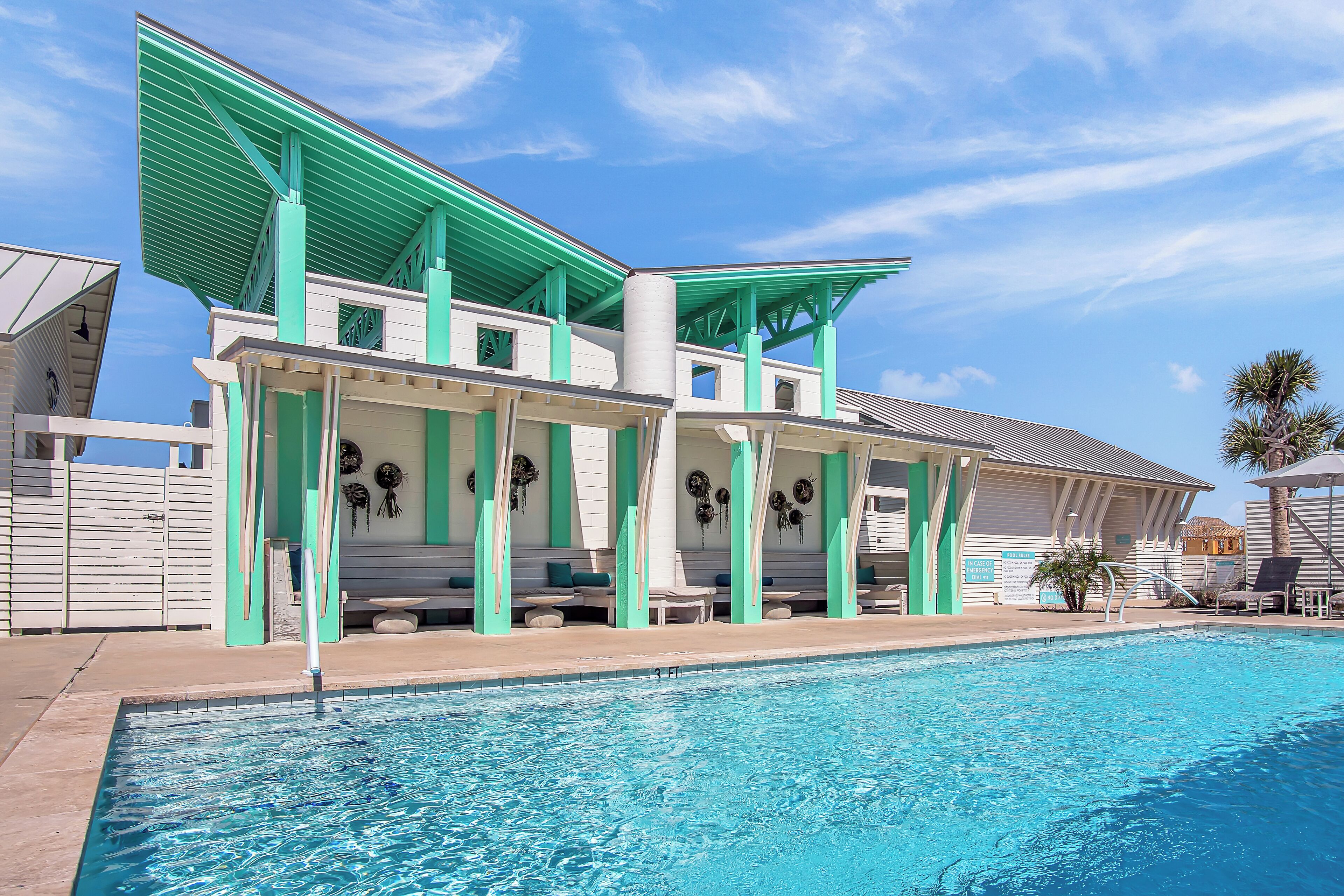 A poolside area with a pool, a covered seating area, and a building with green accents.