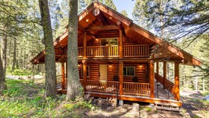 A two-story log cabin with a balcony, surrounded by forest.