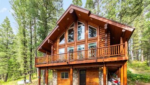 A log cabin with a balcony, stone foundation, and a door.