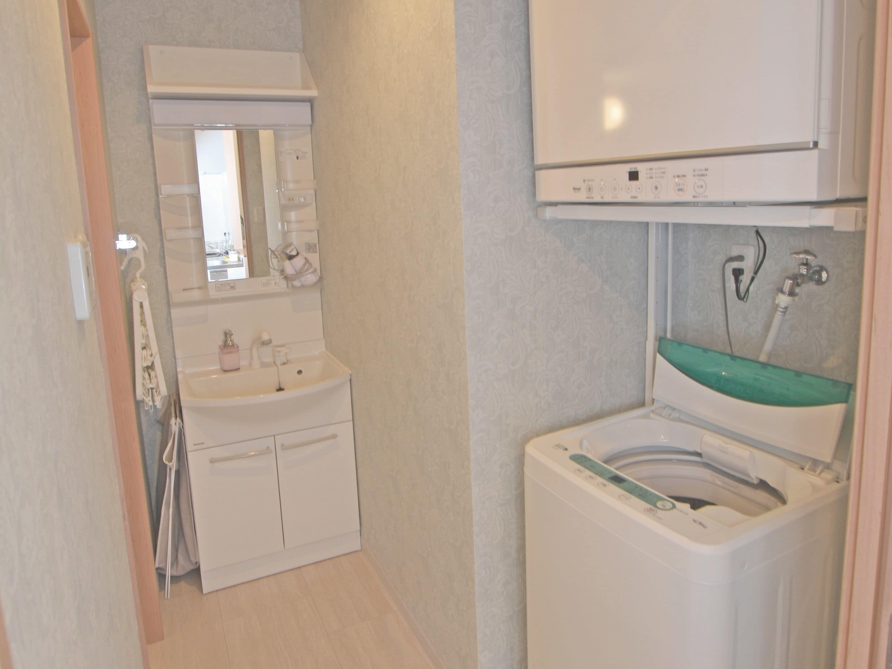 A compact bathroom with a white sink, a mirror above it, and a green-tinted shower enclosure.