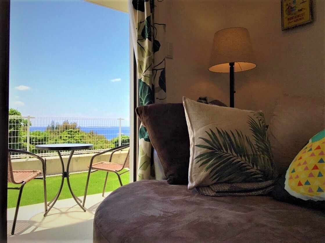 A room with a view of the sea, a sofa, a lamp, and a table with chairs.