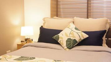 Una cama bien hecha con colcha floral, dos almohadas y una mesita de noche con lámpara y reloj.