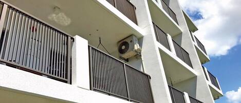 A multi-story building with balconies, air conditioning units, and a clear sky.