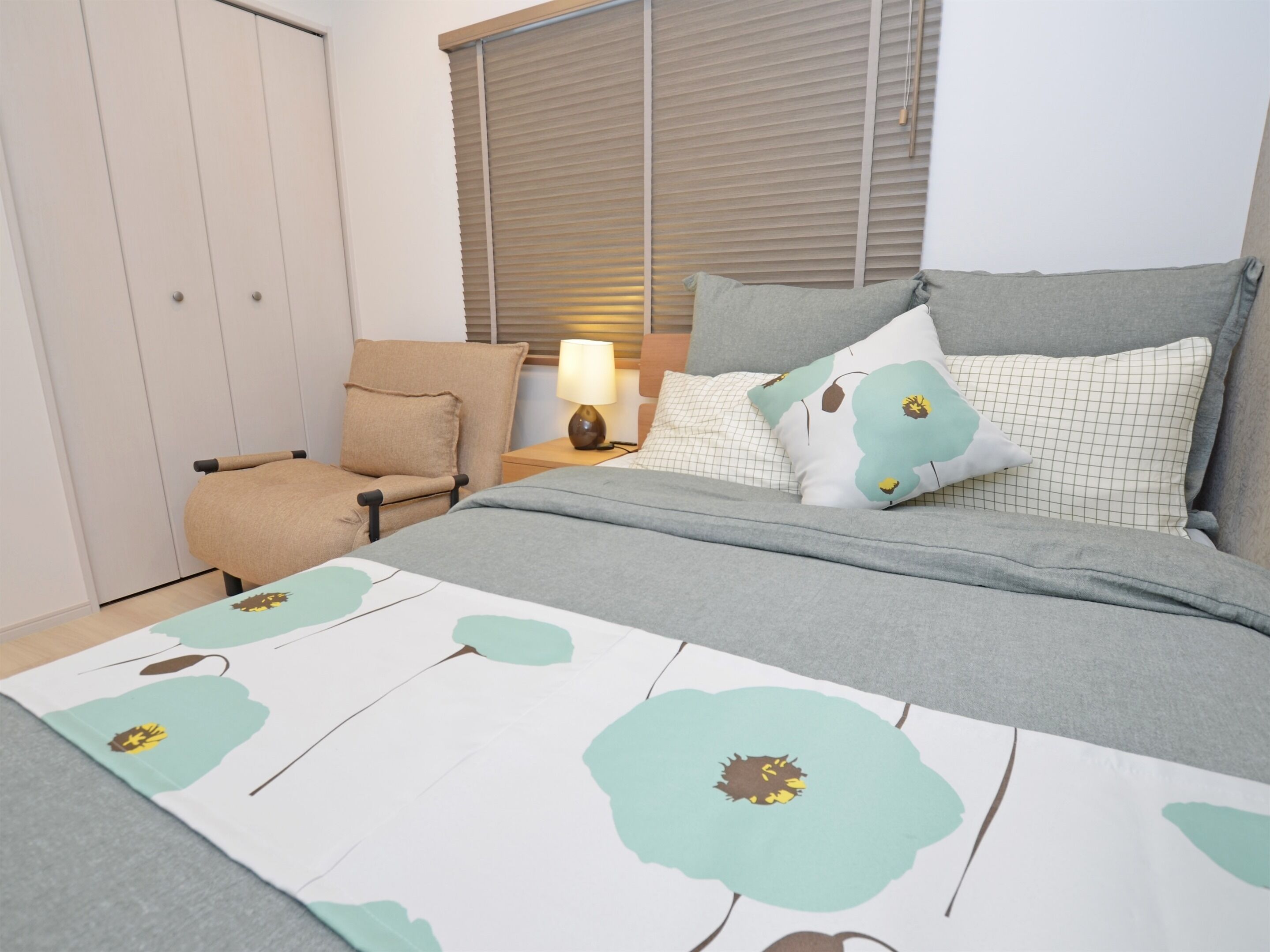 A bedroom with a bed, a chair, a nightstand, and a window with blinds.