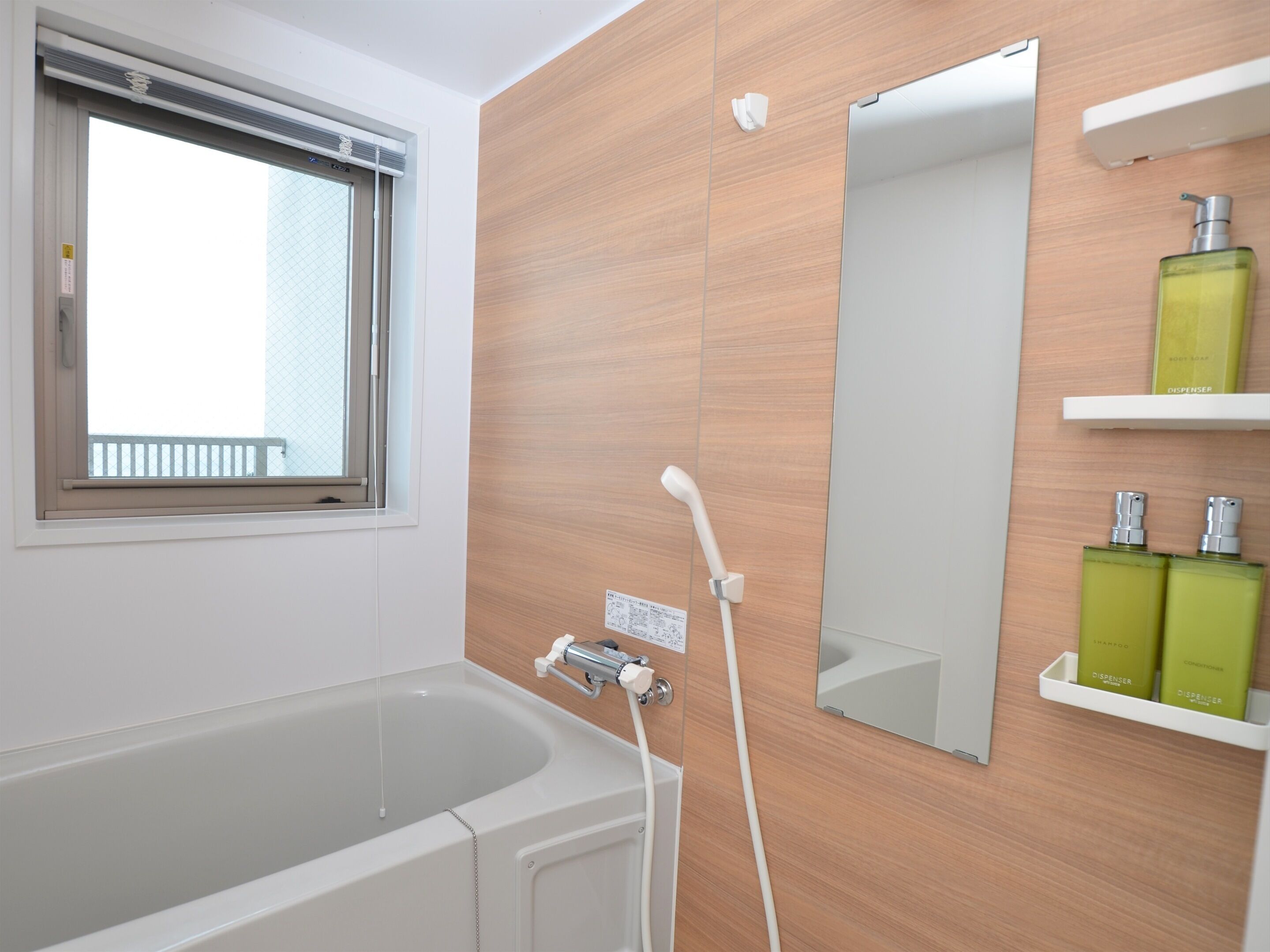 A modern bathroom with a bathtub, a window, a mirror, and a shelf with toiletries.