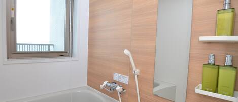 A modern bathroom with a bathtub, a window, a mirror, and a shelf with toiletries.