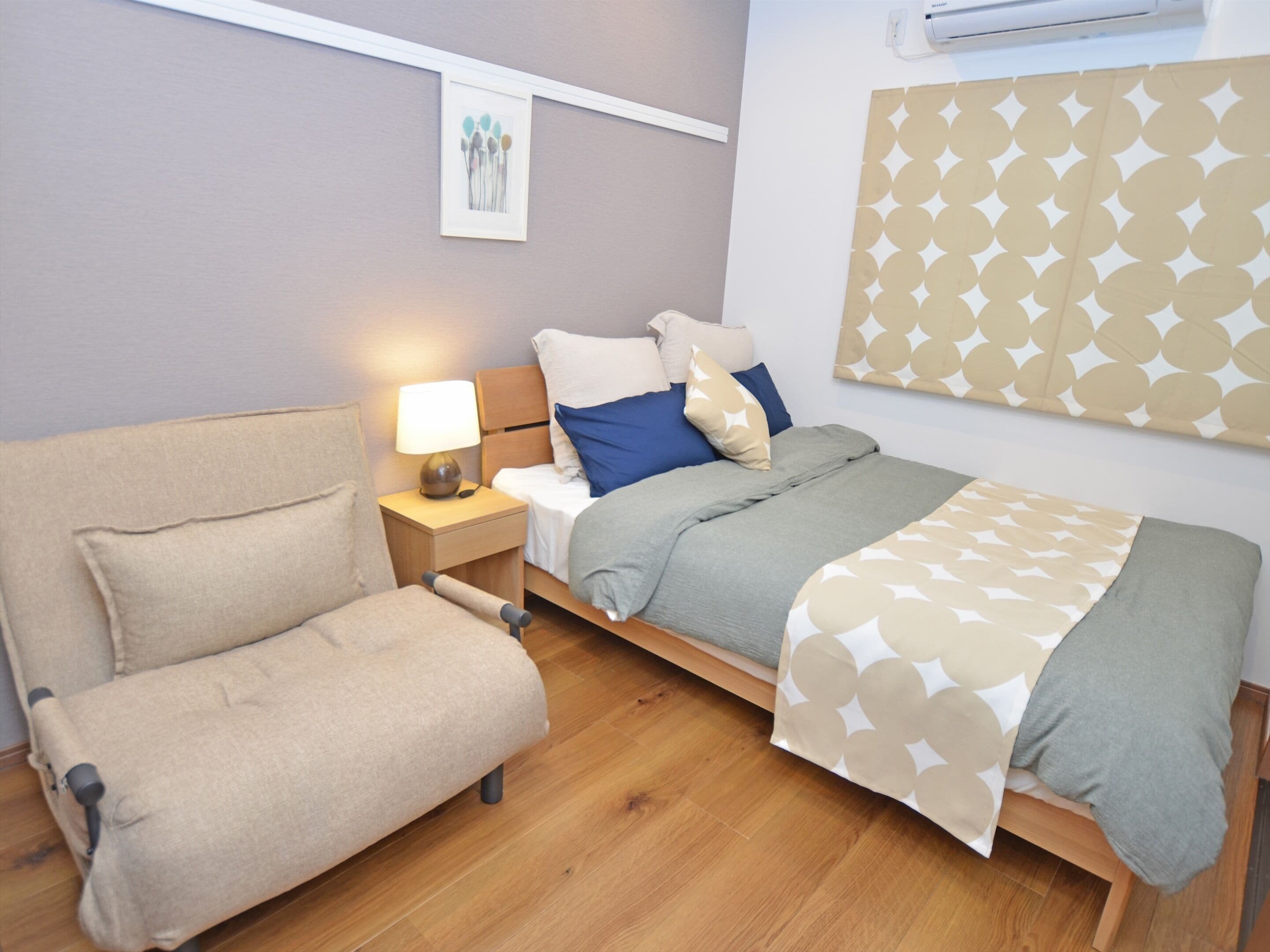 A modern bedroom with a bed, a chair, a nightstand, and a wall-mounted air conditioner.