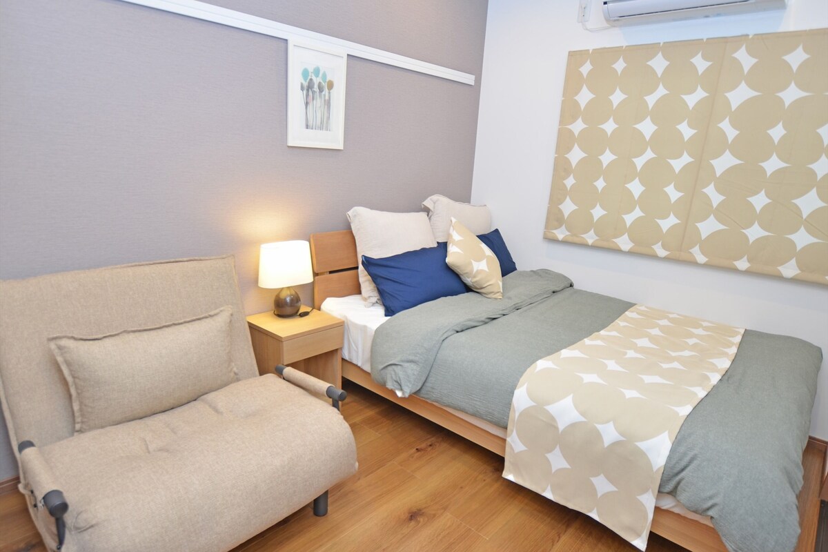 A modern bedroom with a bed, a chair, a nightstand, and a wall-mounted air conditioner.