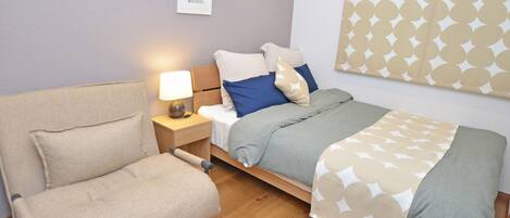 A modern bedroom with a bed, a chair, a nightstand, and a wall-mounted air conditioner.