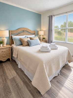 Une chambre à coucher avec un lit, deux tables de chevet, une fenêtre avec des rideaux et une vue sur la verdure à l’extérieur.