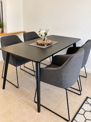 Een moderne eethoek met een rechthoekige tafel, vier grijs gestoffeerde stoelen en een decoratieve vaas met bloemen.