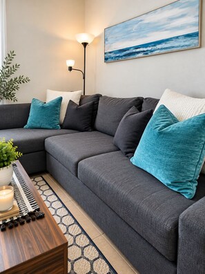 Een moderne woonkamer met een hoekbank, een vloerlamp, een schilderij en een kleine plant.