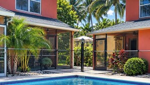 A swimming pool with a tiled edge, surrounded by a covered patio area with glass walls. - Florida Beach Hideaway 2A– Near the Beach • Pool • Fast WiFi • free Parking (Fort Myers)