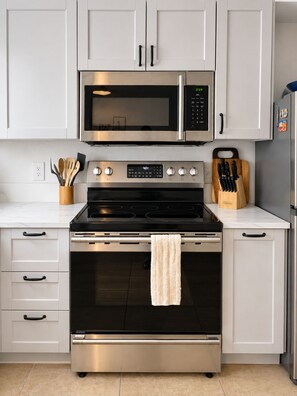 Een keuken met witte kasten, een roestvrijstalen magnetron, een oven en een koelkast.